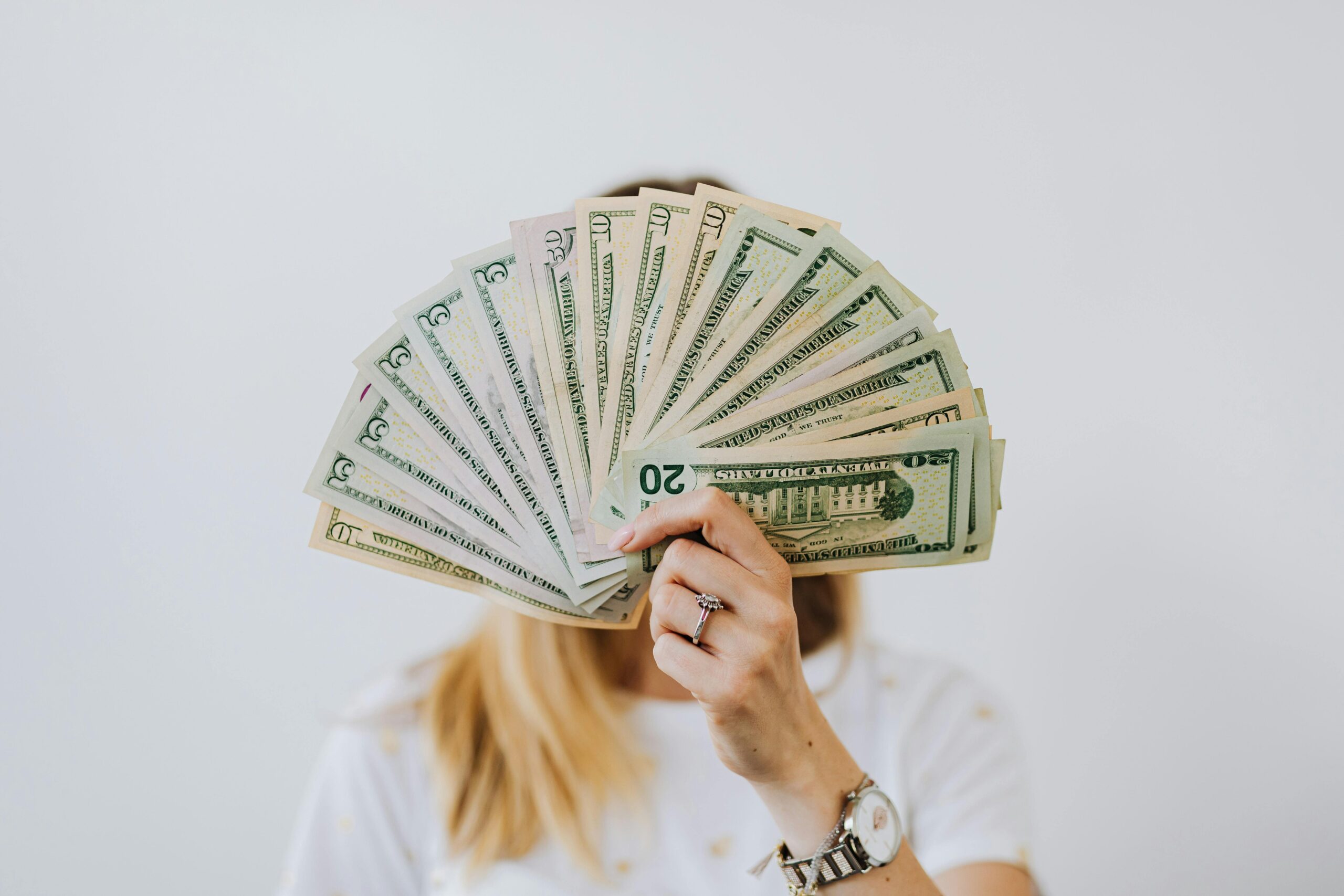 Close-up of a person holding a fan of US dollar bills on a neutral background.